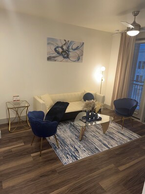 A modern living room with a sofa, two chairs, a coffee table, a painting, and a ceiling fan. - Stylish One-Bedroom Getaway Near Everything (Addison)