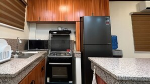 Eine Küche mit Holzschränken, einem schwarzen Kühlschrank, einem eingebauten Backofen, einer Mikrowelle und einem Wasserspender.