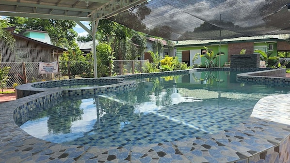 A swimming pool with a tiled edge, surrounded by a covered area with a roof.