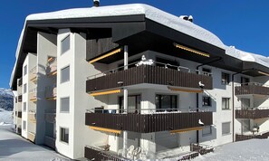 Un immeuble à plusieurs étages, doté de balcons, d’un toit enneigé et surplombant un ciel dégagé.