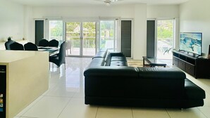 Una sala de estar moderna con un sofá de cuero negro, un comedor con sillas, un televisor y un ventilador de techo.