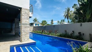 Un edificio moderno con piscina, pilares de piedra y plantas tropicales.