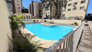 A swimming pool with a white fence, surrounded by potted plants and lounge chairs. - 5 Estrelas - Alto do Bueno (Goiânia)