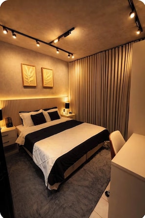 A modern hotel room with a large bed, bedside tables with lamps, a desk, and a curtain-covered window. - 5 Estrelas - Alto do Bueno (Goiânia)