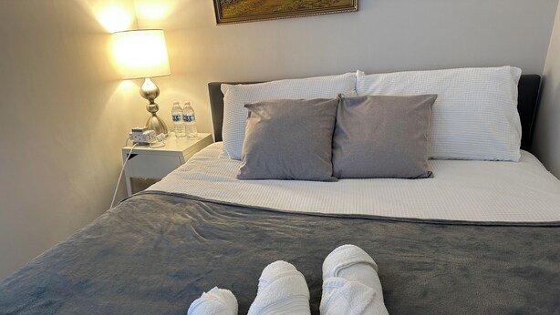 Una cama bien hecha con almohadas, una mesita de noche con lámpara y dos toallas sobre la cama.