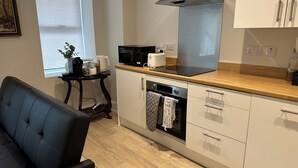 Una cocina moderna con microondas, tostadora y horno, un comedor con una silla y una ventana con persianas.