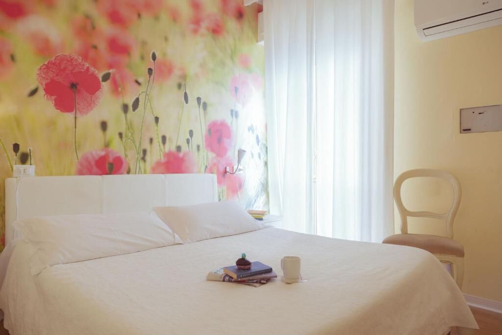 A bedroom with a bed, a chair, a wall-mounted air conditioner, and a window with curtains.