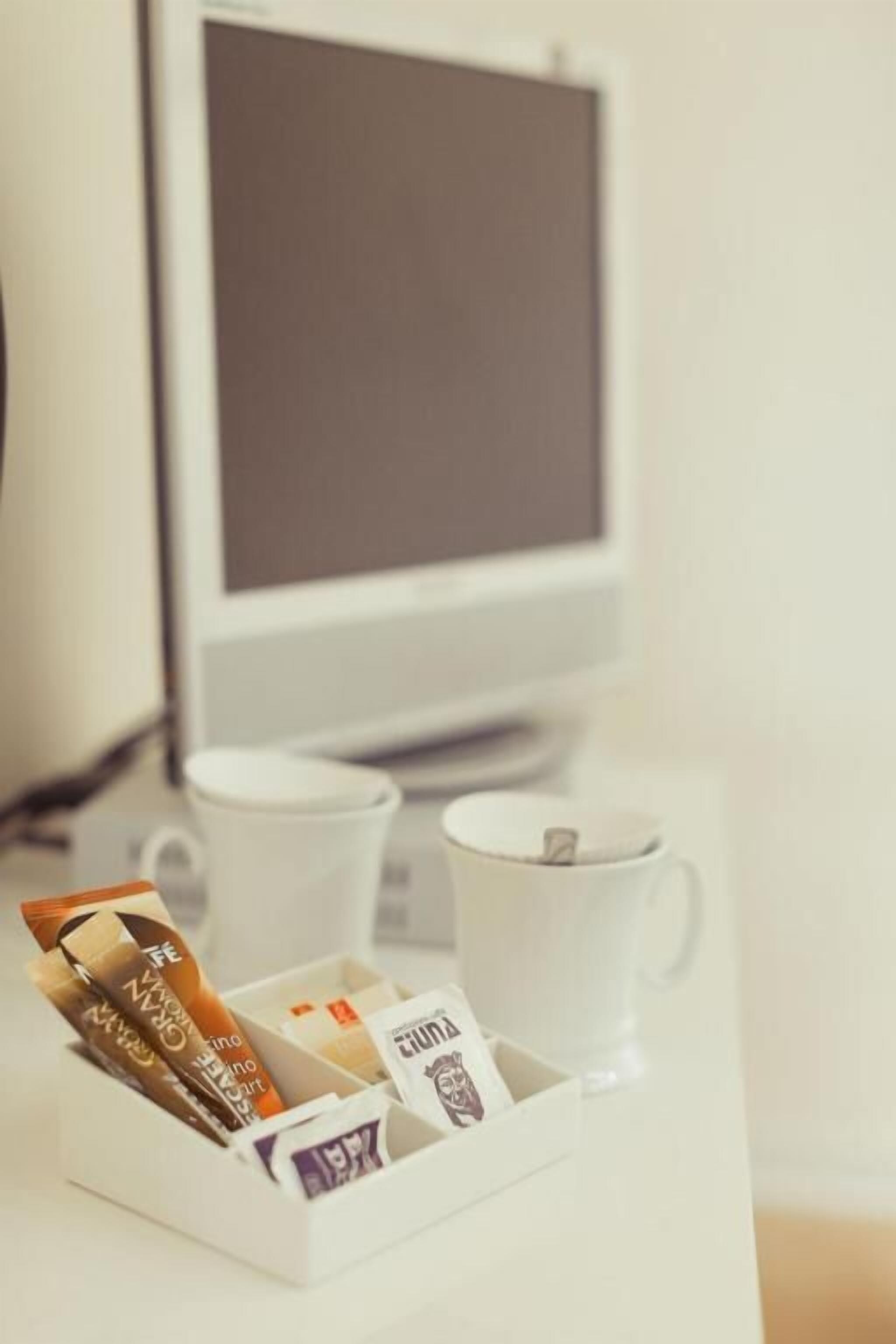 A white desk with a white mug, a white cup, and a white tray holding coffee packets.