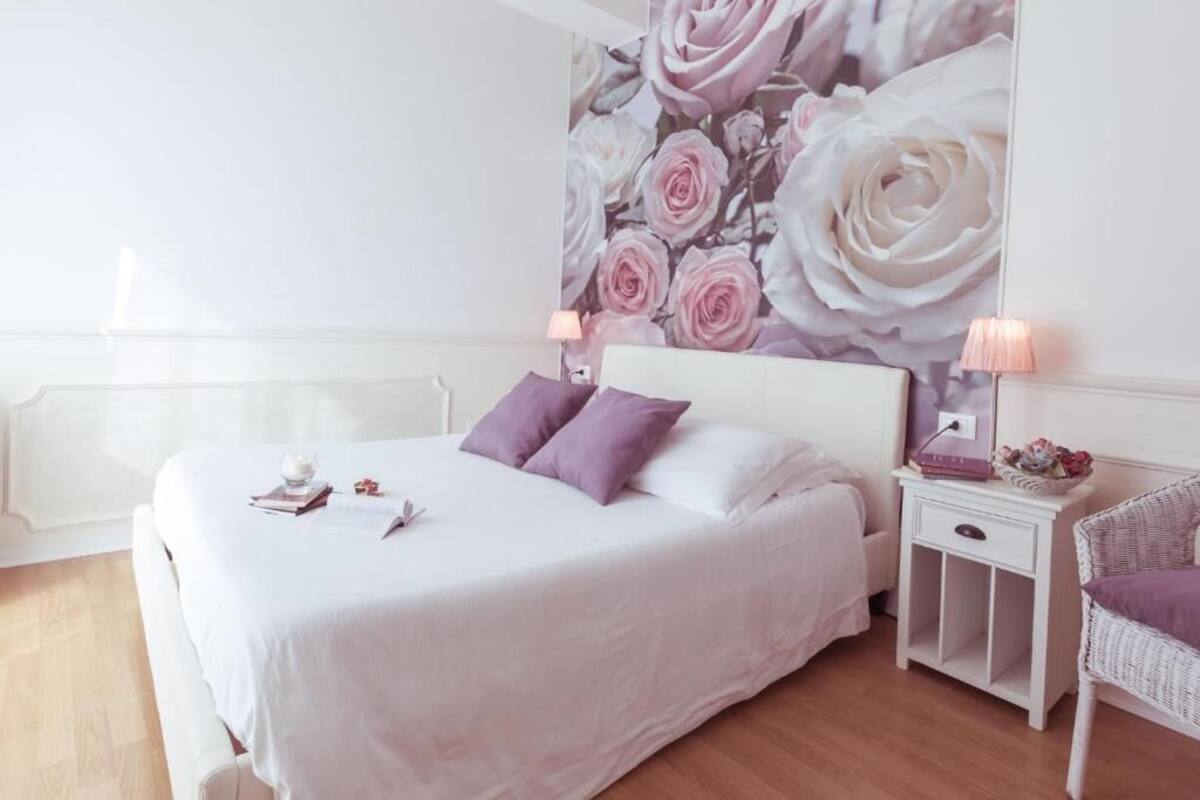 A bedroom with a bed, two bedside tables, a nightstand, a chair, and a floral wall mural.