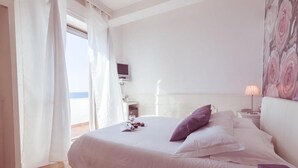 Un dormitorio con cama, mesita de noche, lámpara, televisión y vistas al exterior.
