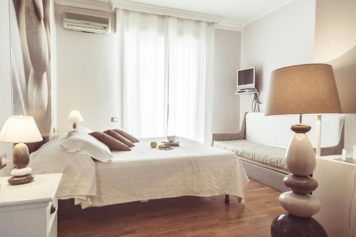 A hotel room with a bed, bedside tables, a TV, a lamp, and a window with curtains.