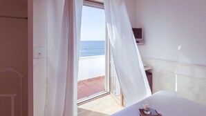 Un dormitorio con cama, mesita de noche con lámpara, televisor y vistas al mar a través de una ventana.