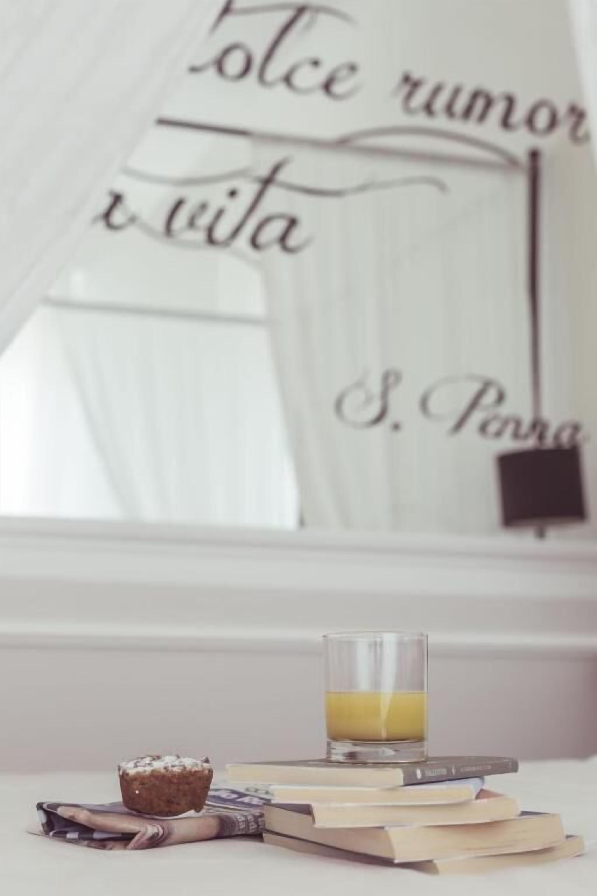Un verre de jus d’orange posé sur une pile de livres, à côté d’un muffin, et un miroir orné d’une citation.
