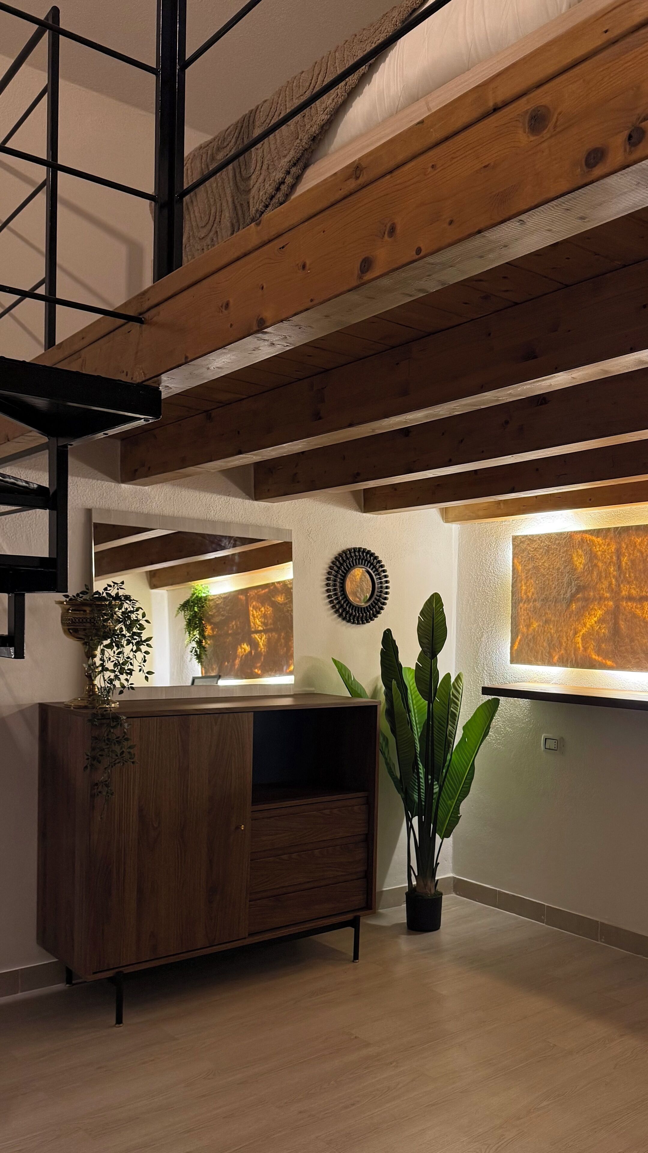 A room with a wooden ceiling, a dark wooden cabinet, a large potted plant, and a wall with a textured artwork.