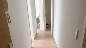 En hall med trägolv, vita väggar och en dörr på vänster sida.