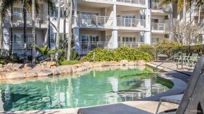 Ein mehrstöckiges Hotel mit Swimmingpool, Palmen und einem angelegten Garten.