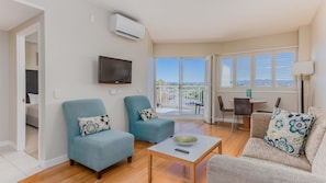 Ein Wohnzimmer mit zwei Sesseln, einem Sofa, einem Fernseher und einem Balkon mit Blick.