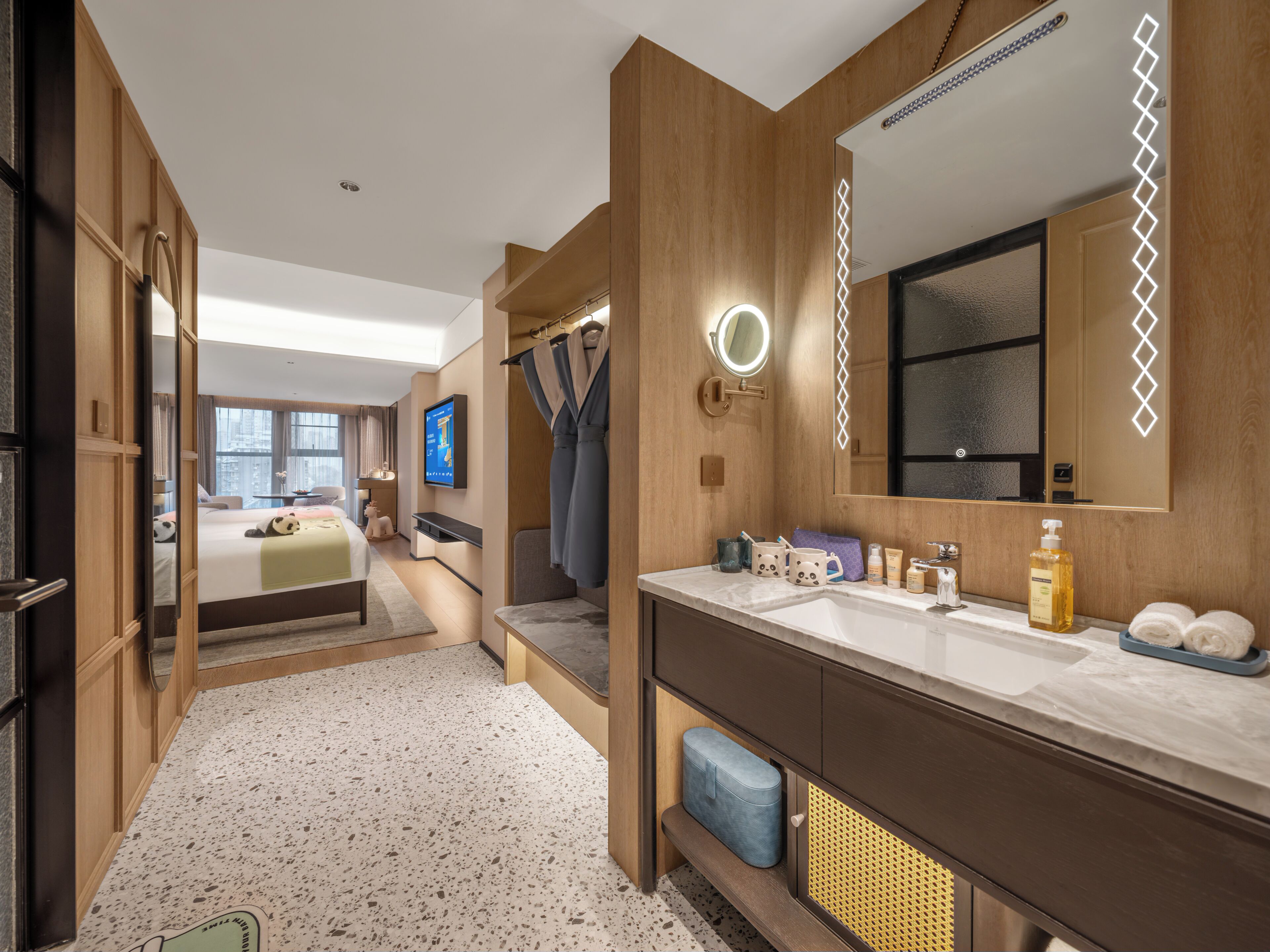 A modern hotel room with a large bed, a separate bathroom, a TV, and a mirror with lights.