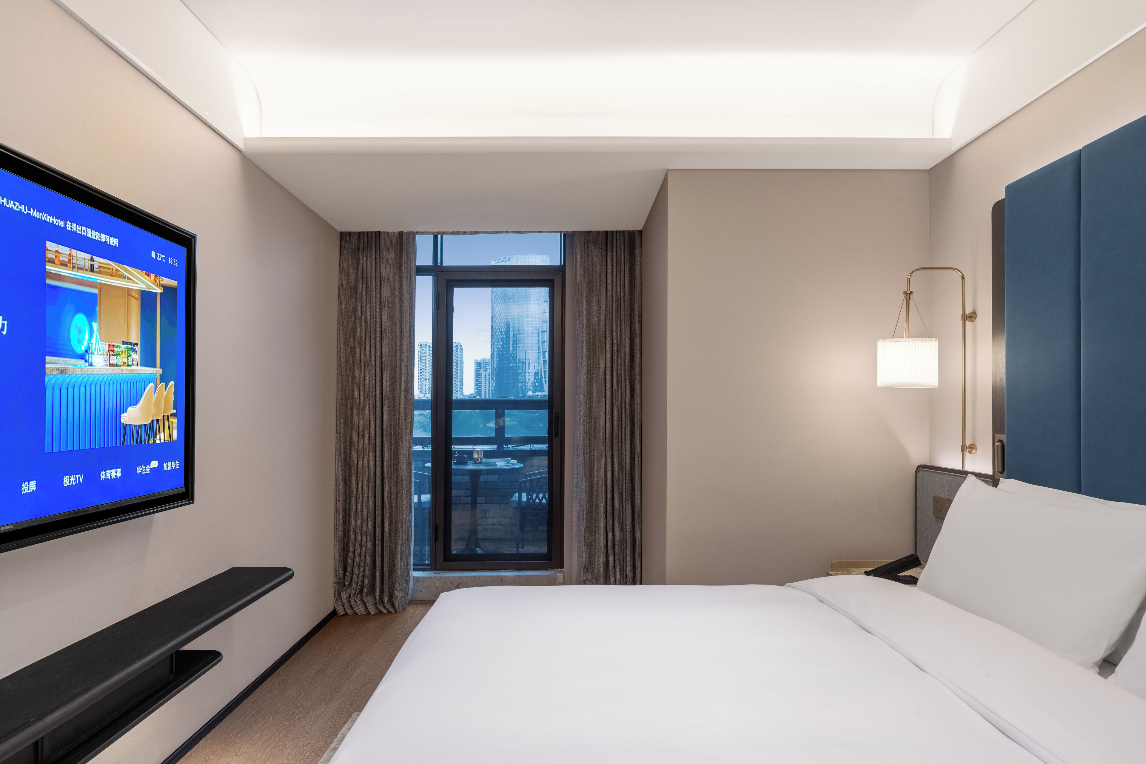 Een hotelkamer met een bed, een aan de muur bevestigde televisie, een raam met gordijnen en een nachtkastje met een lamp.