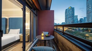 Habitación de hotel con balcón, cama, mesita con frutero y vistas a la ciudad.