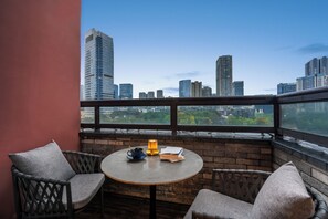 En balkon med udsigt over byens skyline, et rundt bord med en bog og et lys, samt to fletstole.