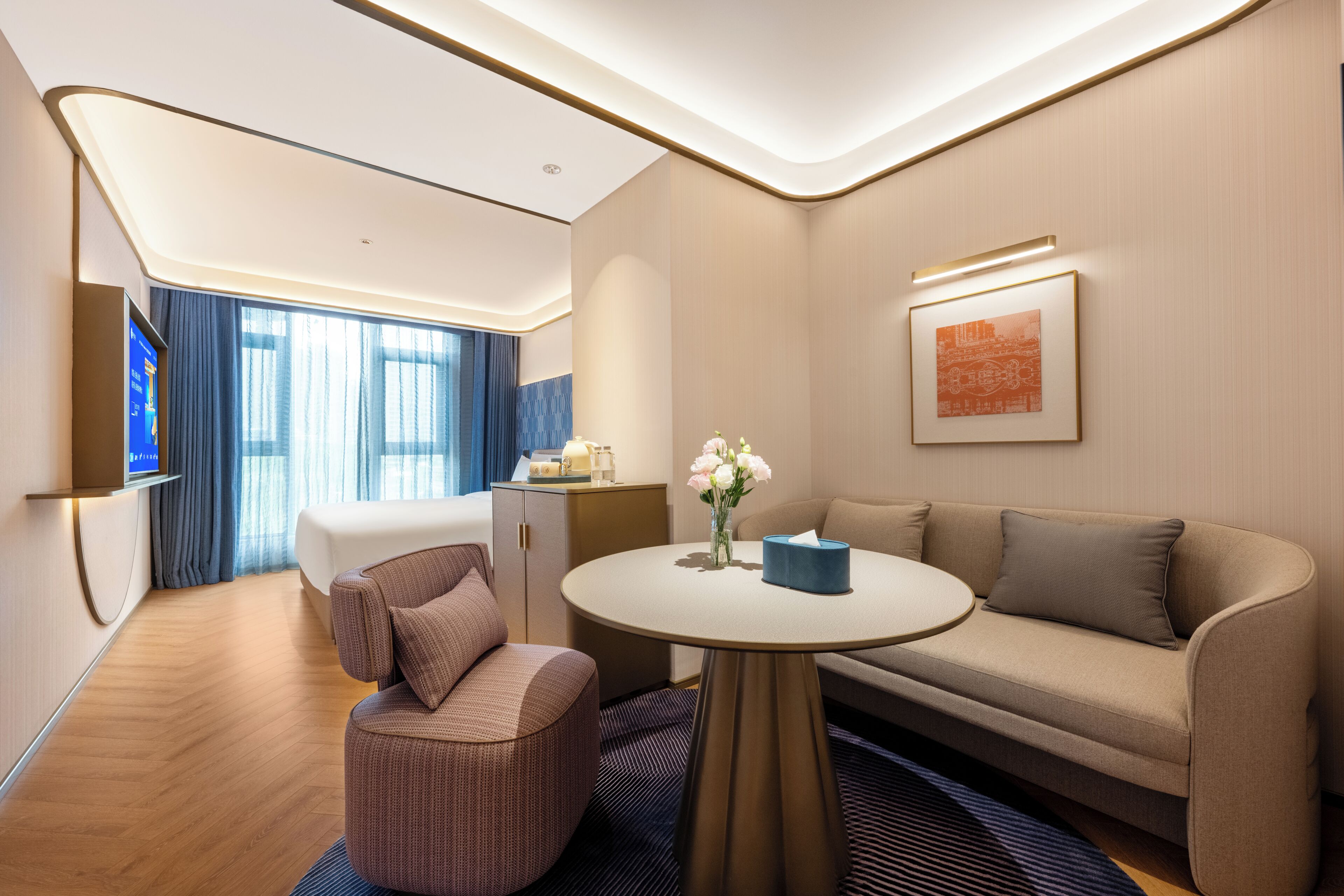 Een moderne hotelkamer met een bank, fauteuil, rond tafel en een flatscreen televisie.