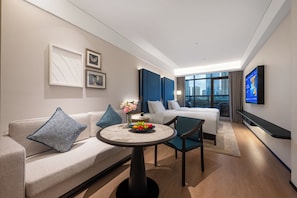 A modern hotel room with a sofa, a bed, a dining table with fruit, a TV, and a city view. - Manxin Hotel Chengdu Taikoo Li JiuyanBridge (Chengdu)