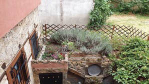 A stone wall with a metal gate, a small garden with various plants, and a brick structure with a circular opening.