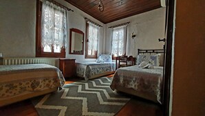 A bedroom with two beds, a wooden ceiling, a radiator, lace curtains, and a patterned rug.