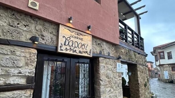 A building with a stone facade, a black door with a sign above it, and a small balcony.