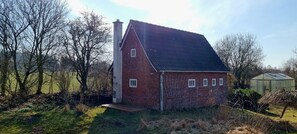Een bakstenen huis met een schuin dak, schoorsteen en een kleine tuin.