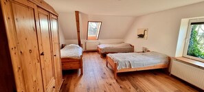Een slaapkamer met twee houten bedden, een houten garderobe, een dakraam en een raam met uitzicht op groen.
