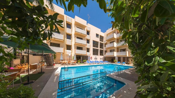 Un hotel con piscina circondata da lettini e ombrelloni, una scala e un edificio a più piani con balconi.