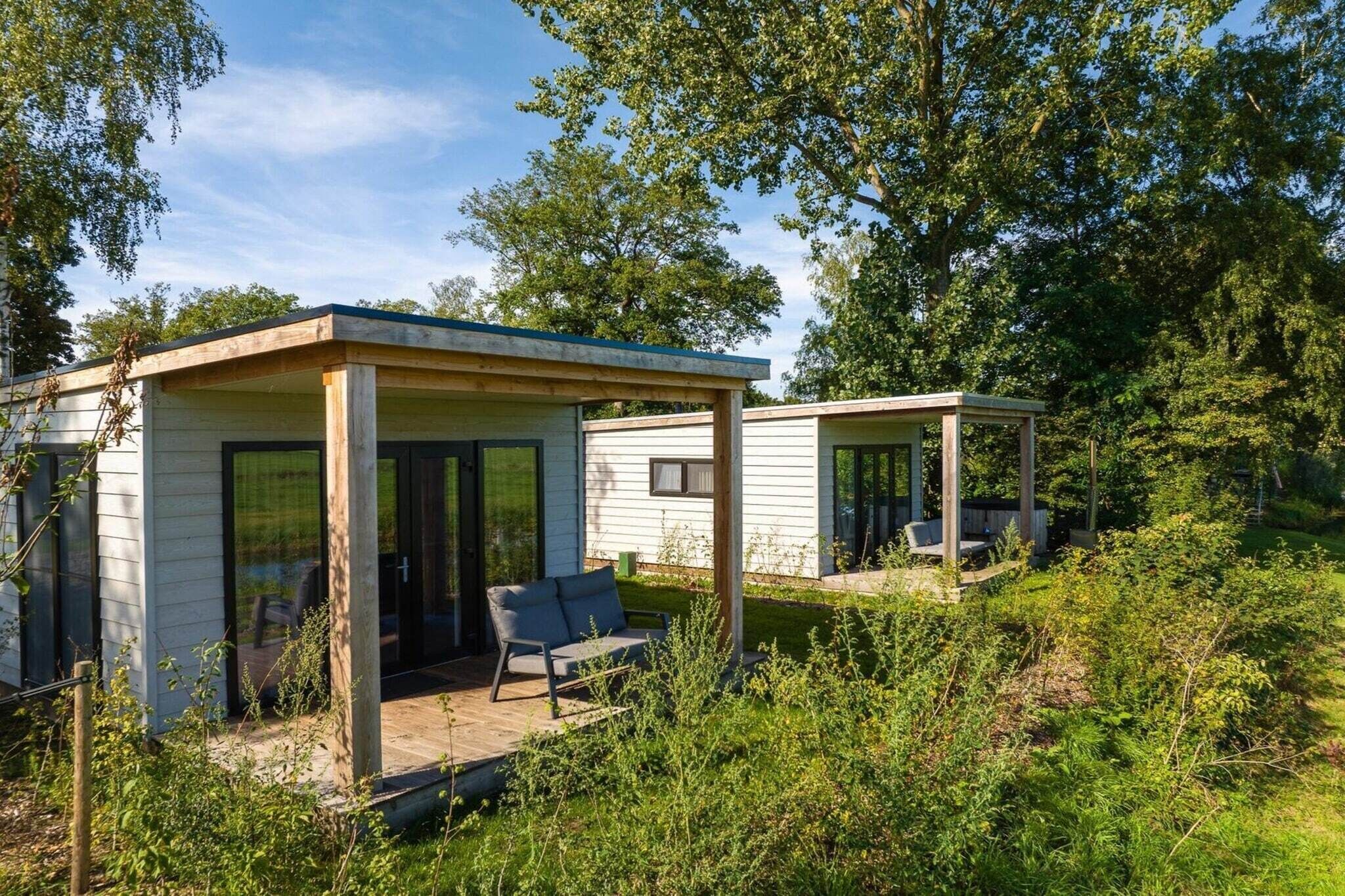 Deux petites cabanes à un seul étage, dotées de portes et de fenêtres en verre, et entourées de verdure.