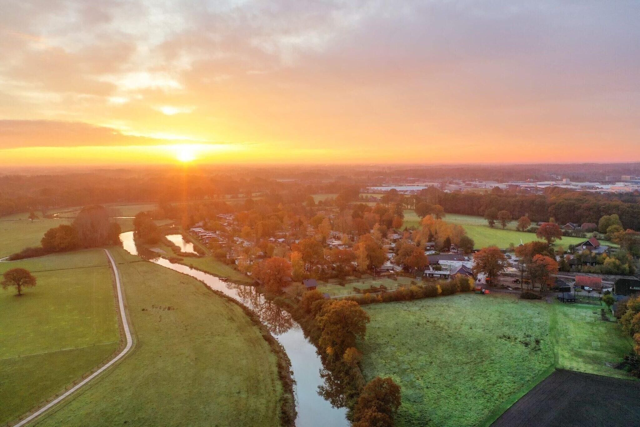 Vista aérea de una zona rural con campos, un río y casas al atardecer.