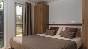 Een slaapkamer met een groot bed, een houten garderobe en een schuifdeur naar een balkon.