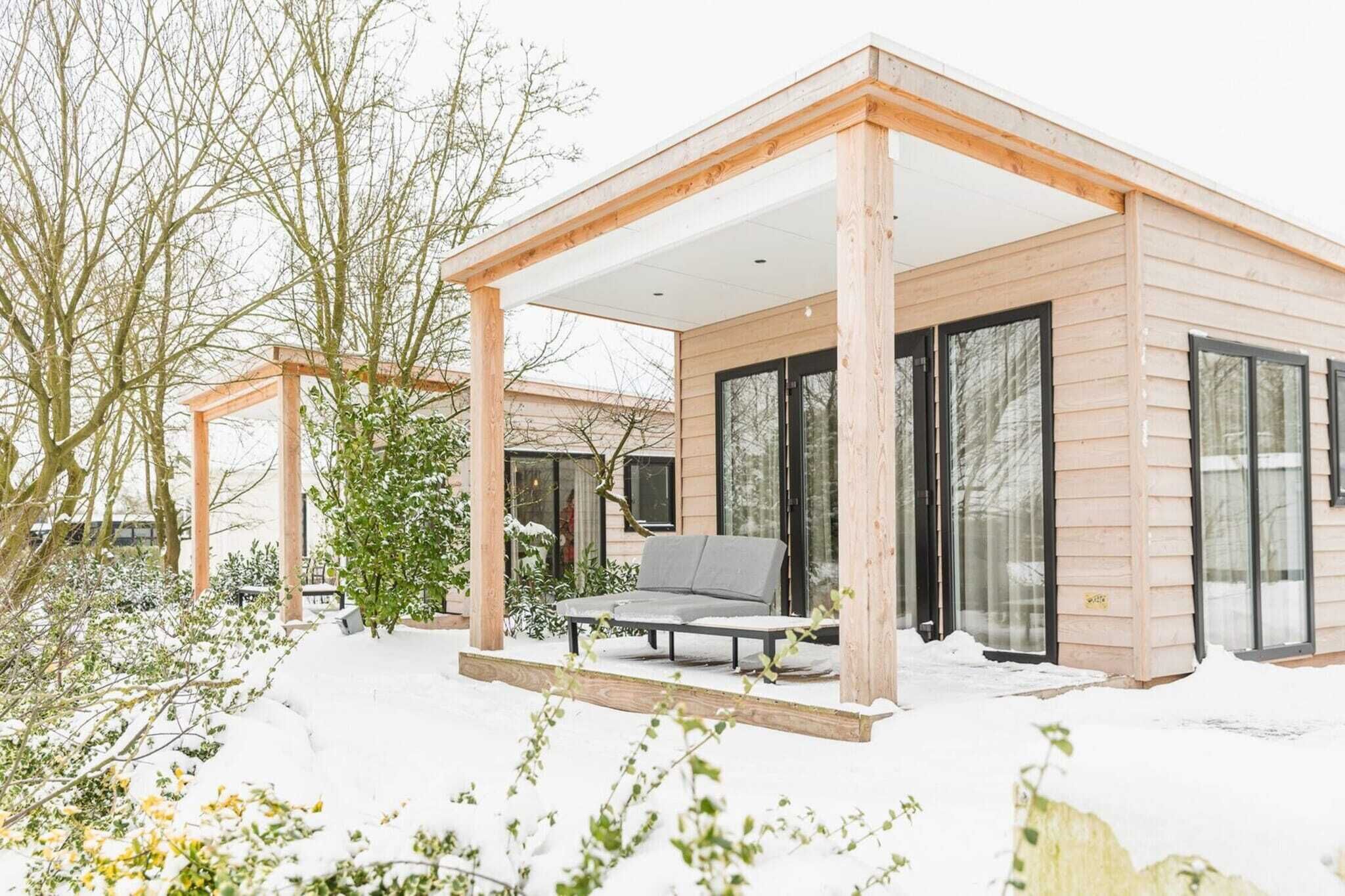 Eine moderne Holzhütte mit überdachter Terrasse, großen Fenstern und einer Sitzecke.