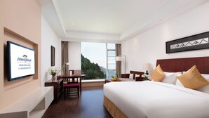 A hotel room with a bed, desk, chair, TV, and a view of the outdoors. - Howard Johnson Lushan Jiahao (Jiujiang)