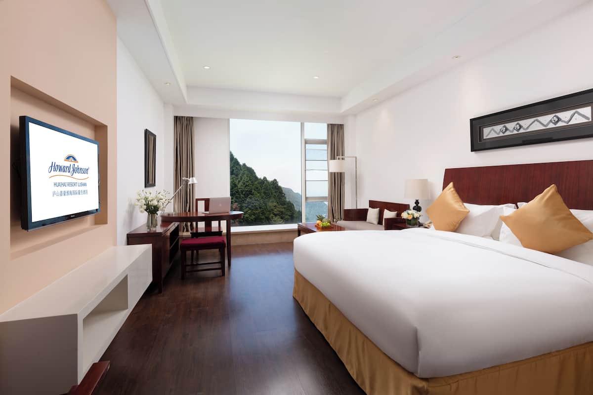 Habitación de hotel con cama, escritorio, silla, televisor y vistas al exterior.