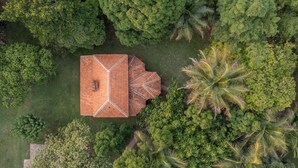 An aerial view of a building with a distinct geometric roof structure surrounded by dense greenery. - Coffee Cottage by Raho Stream View Estate Escape (Coorg)