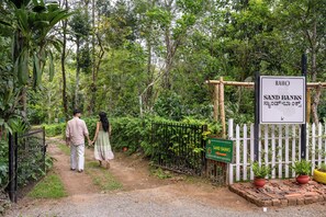 A pathway leading to a sign for 'RAHO SAND BANKS' with a white picket fence and potted plants.