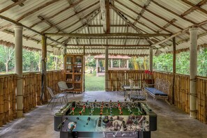 A covered outdoor area with a foosball table, seating, and a view of a garden.
