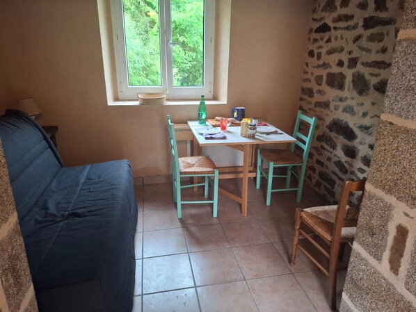 A small room with a window, a table with chairs, a sofa, and a stone wall.