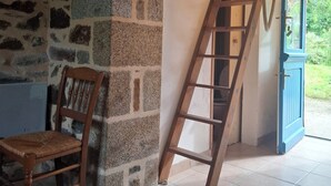 A room with a stone wall, a wooden chair, a wooden ladder, and a blue door leading outside.
