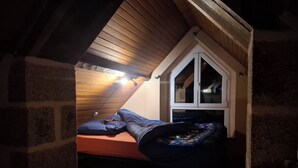 A small attic bedroom with a sloped ceiling, a window, and a bed.