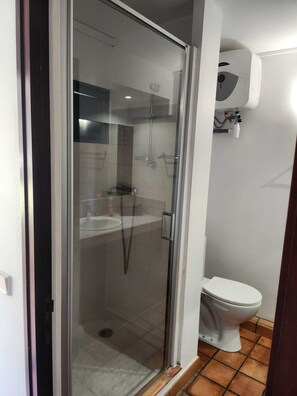 Ein Badezimmer mit einer Duschkabine, einer weißen Toilette und einem sichtbaren Warmwasserbereiter.