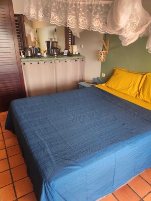 A room with a bed, a green wall, a window with a curtain, a small table with a lamp, and a wall-mounted shelf with various items. - Charming air-conditioned studio with sea view, unoverlooked terrace, beach 1 min -Tartane (Tartane)