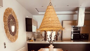 Zona pranzo con tavolo in legno, sedie, lampadario intrecciato e una cucina sullo sfondo.