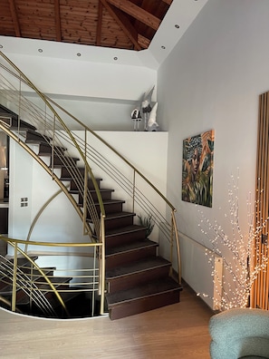 A modern interior with a spiral staircase, wooden beams, a painting, and a decorative plant.