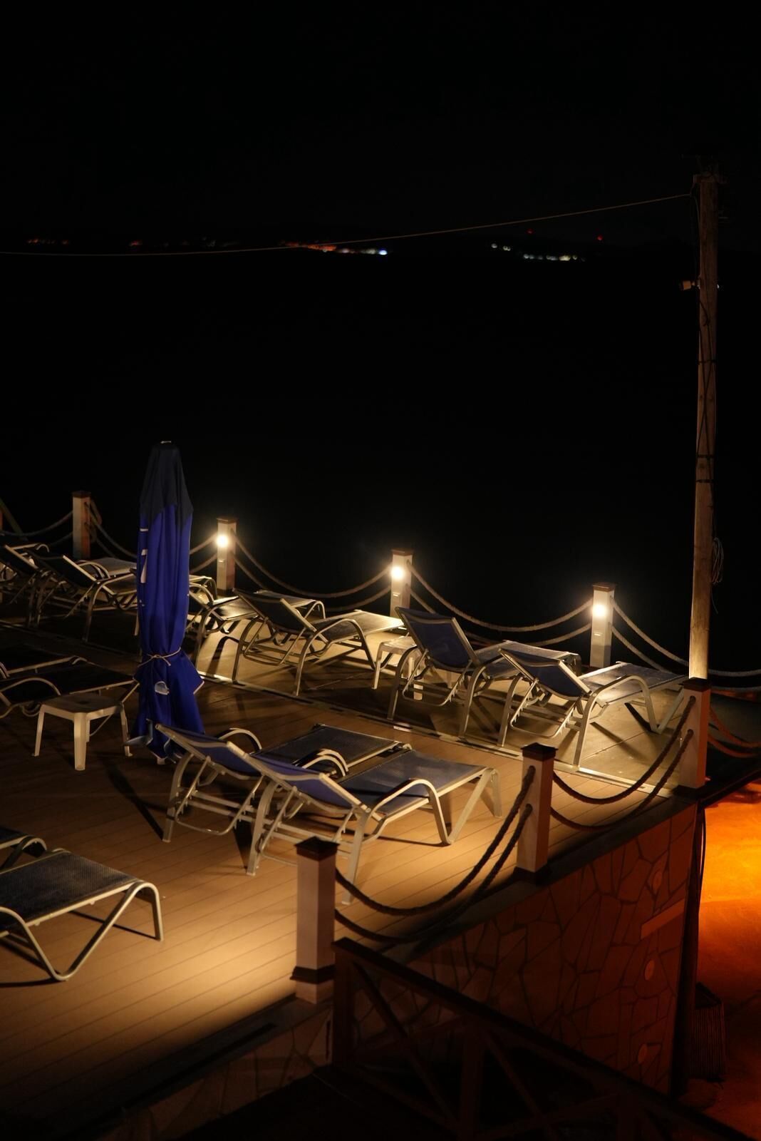 A rooftop lounge area with sun loungers and umbrellas, surrounded by a wooden deck.